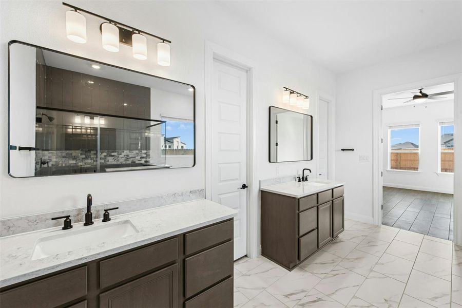 Bathroom with a shower stall, two vanities, light marble finish floors, and a ceiling fan