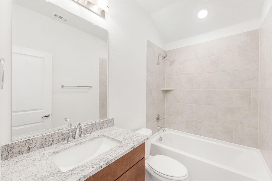 Bathroom with granite countertop vanity, tub-shower combo with tile surround, and wood cabinet base