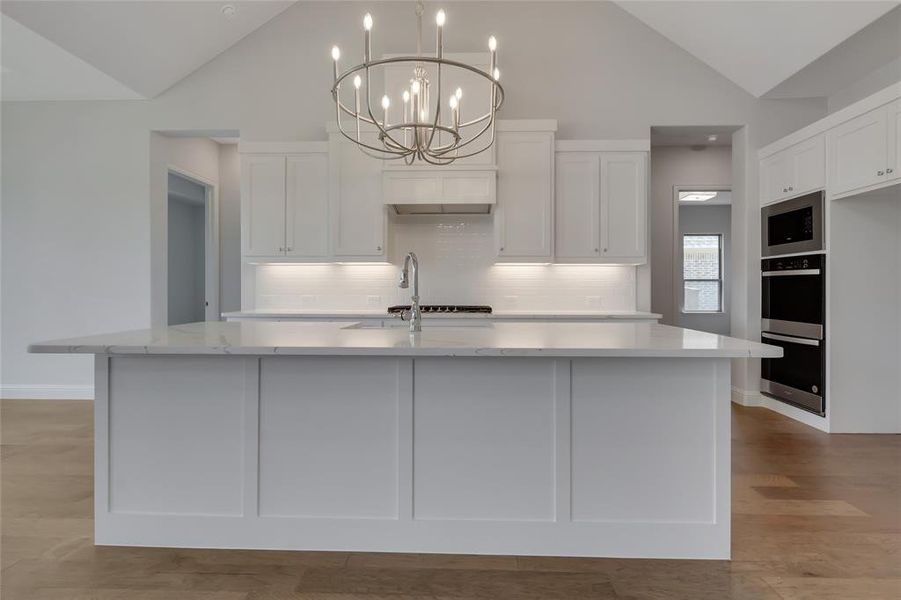 Kitchen featuring decorative light fixtures, stainless steel appliances, tasteful backsplash, a center island with sink, and light wood-type flooring