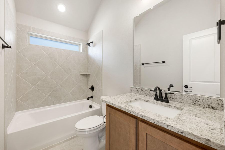Bathroom with granite vanity, wood cabinets, tub-shower combo with diagonal tile, and black fixtures