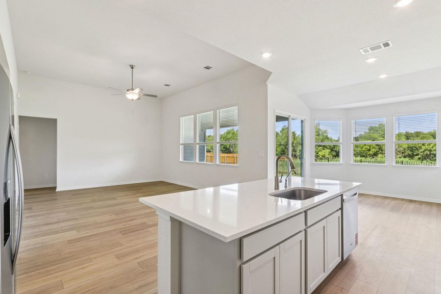 Kitchen with open floor plan, an island with sink, light wood finished floors, light stone counters, and a ceiling fan Kitchen with open floor plan, an island with sink, light wood finished floors, light stone counters, and a ceiling fan