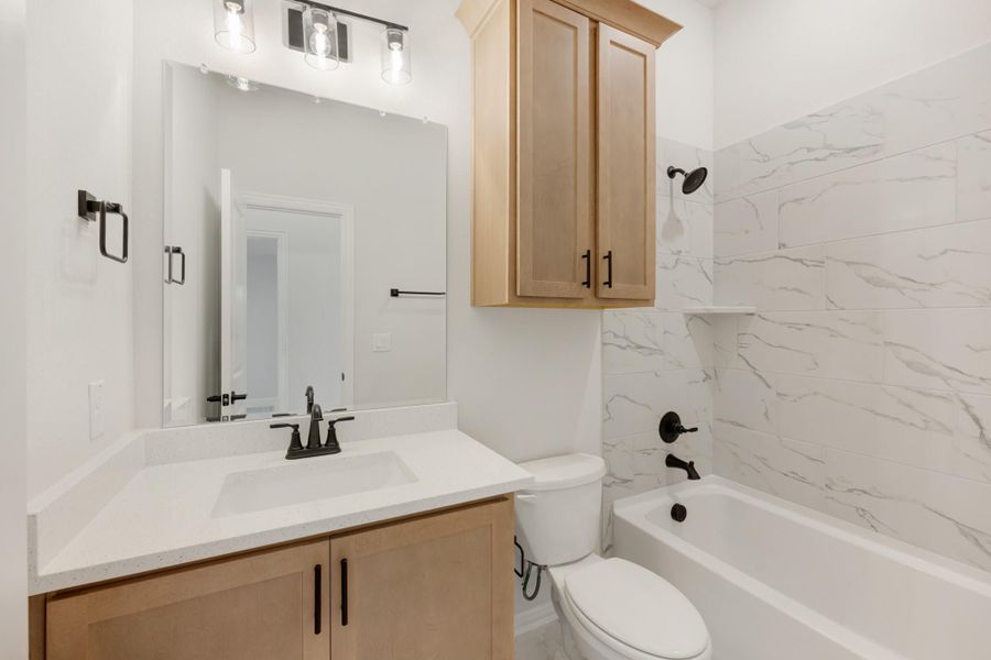 Bathroom with light wood vanity, white quartz countertop, and tub with marble-style tile surround