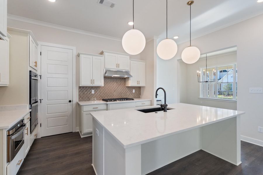 Kitchen featuring an island with sink, tasteful backsplash, light quartz counters, decorative light fixtures, and white cabinets Kitchen featuring an island with sink, tasteful backsplash, light quartz counters, decorative light fixtures, and white cabinets