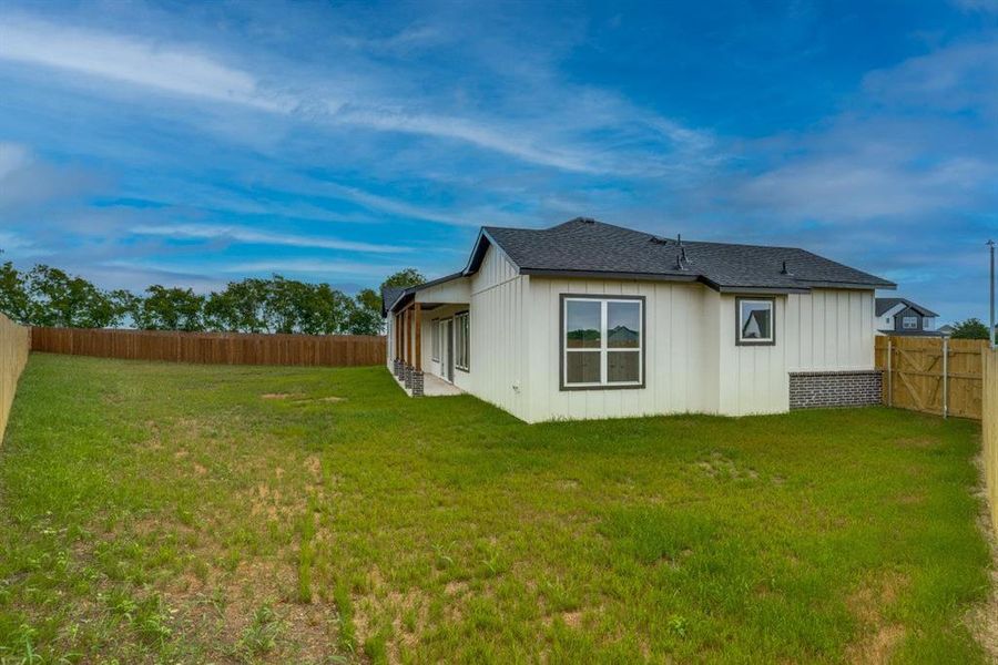 Expansive fenced backyard featuring a white siding exterior with dark trim, a covered patio with wood columns, and a dark shingled roof Expansive fenced backyard featuring a white siding exterior with dark trim, a covered patio with wood columns, and a dark shingled roof