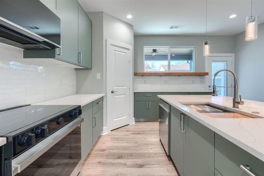 Kitchen with ventilation hood, sink, decorative backsplash, appliances with stainless steel finishes, and light stone counters