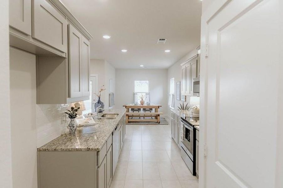 Kitchen with appliances with stainless steel finishes, light stone counters, recessed lighting, backsplash, and light tile patterned floors Kitchen with appliances with stainless steel finishes, light stone counters, recessed lighting, backsplash, and light tile patterned floors