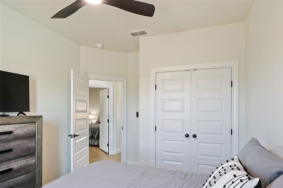 Bedroom featuring a ceiling fan, white paneled doors with black hardware, and light-toned walls