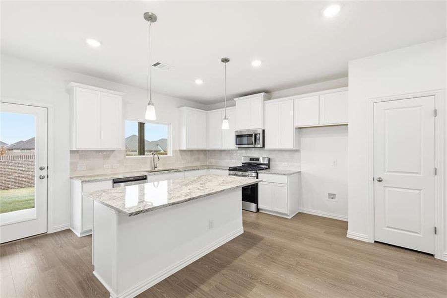 Kitchen featuring stainless steel appliances, white cabinets, decorative light fixtures, a kitchen island, and recessed lighting