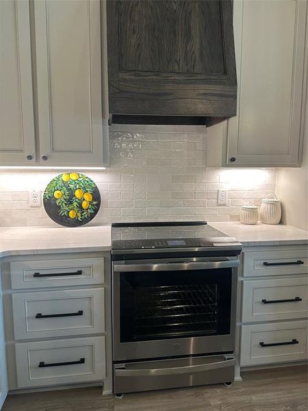 Contemporary kitchen featuring a stainless steel range, light-toned shaker cabinets, and a custom wood-paneled range hood