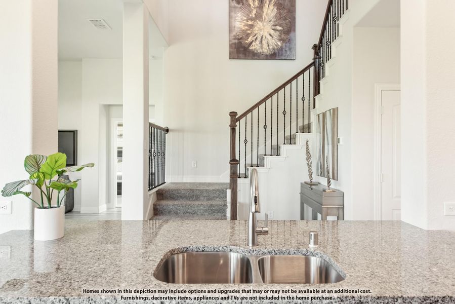 Kitchen island with granite countertop and stainless steel sink overlooking open living area with staircase and high ceilings