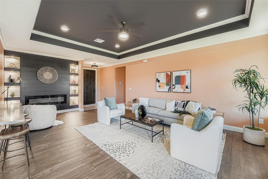Living room featuring a fireplace, ornamental molding, hardwood / wood-style floors, a ceiling fan, and a tray ceiling