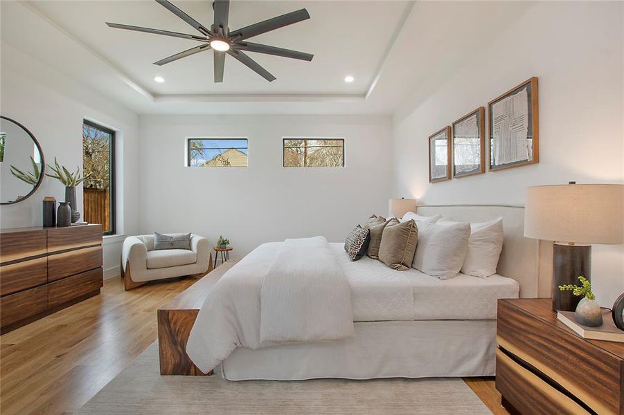 Bedroom with a tray ceiling, ceiling fan, and light hardwood / wood-style flooring