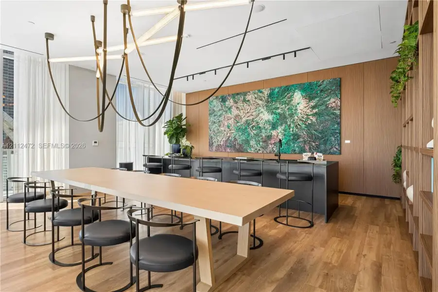Wood-finish flooring, custom wood wall paneling, built-in shelving, architectural linear chandelier, and integrated black countertop with matte finish faucet