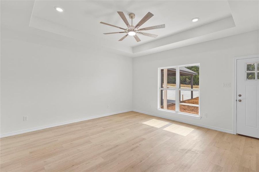 Empty room with a raised ceiling, light wood finished floors, recessed lighting, and ceiling fan Empty room with a raised ceiling, light wood finished floors, recessed lighting, and ceiling fan