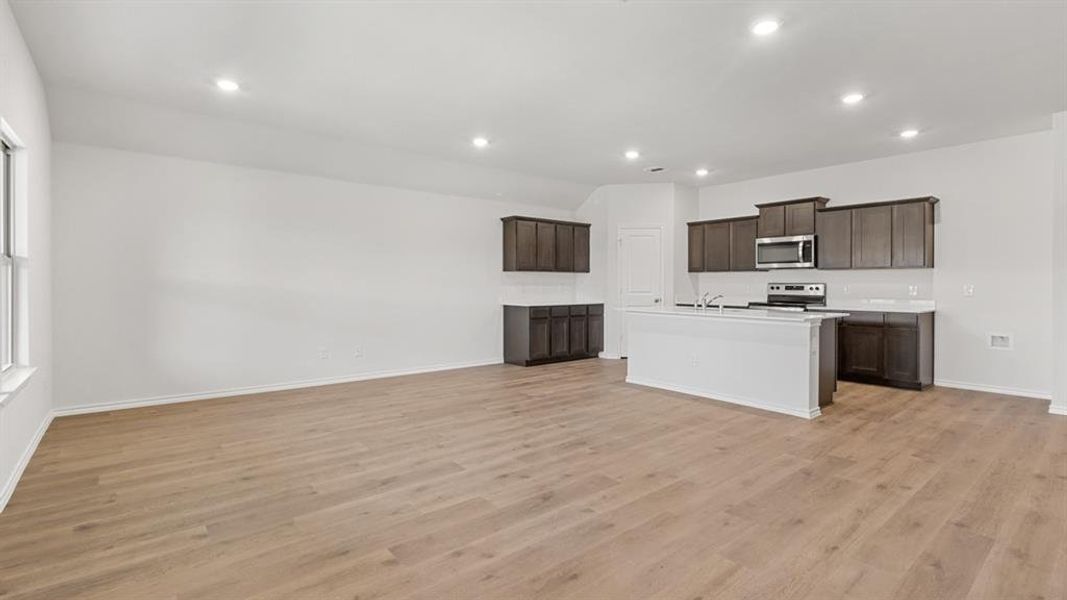 Kitchen featuring light countertops, dark wood finish cabinetry, stainless steel appliances, an island with sink, and open floor plan
