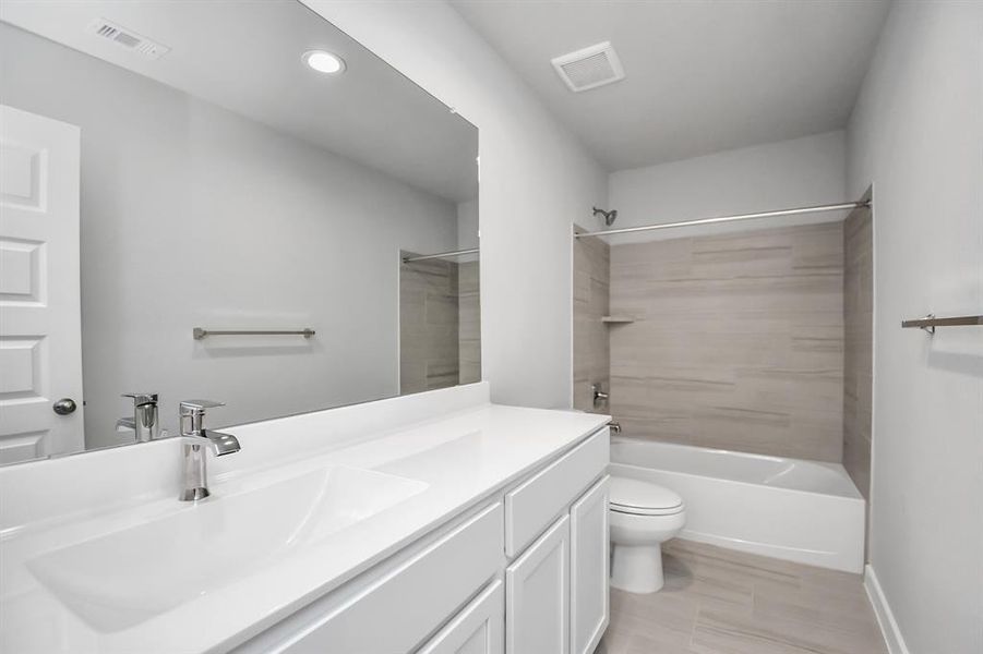 The secondary bath boasts stylish tile flooring, a bath/shower combo with a sleek tile surround, light wood cabinets, and a stunning light countertop.