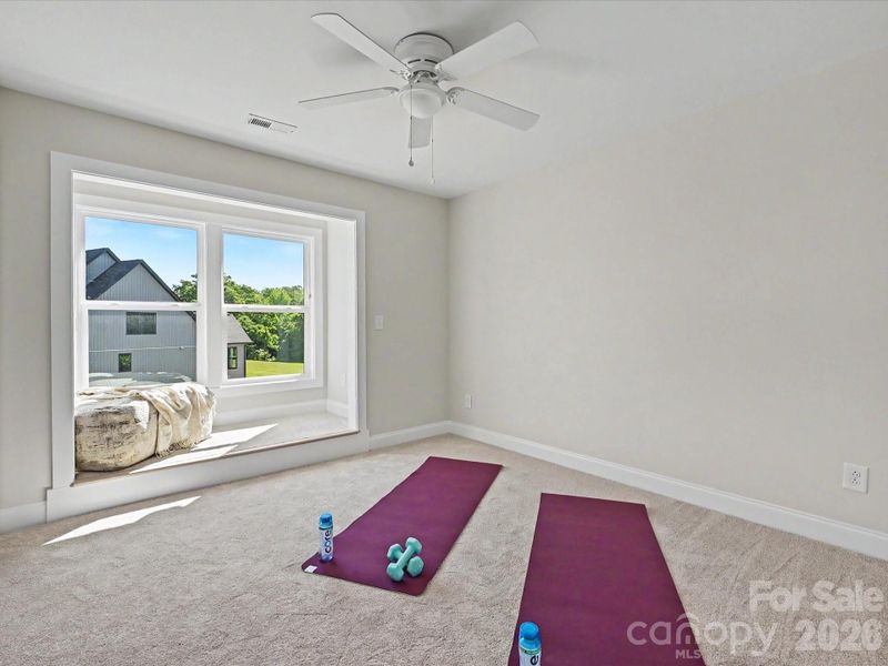 Bright secondary bedroom offers plush carpeting, a charming window seat, and flexible space ideal for guests, a home office, or fitness area.