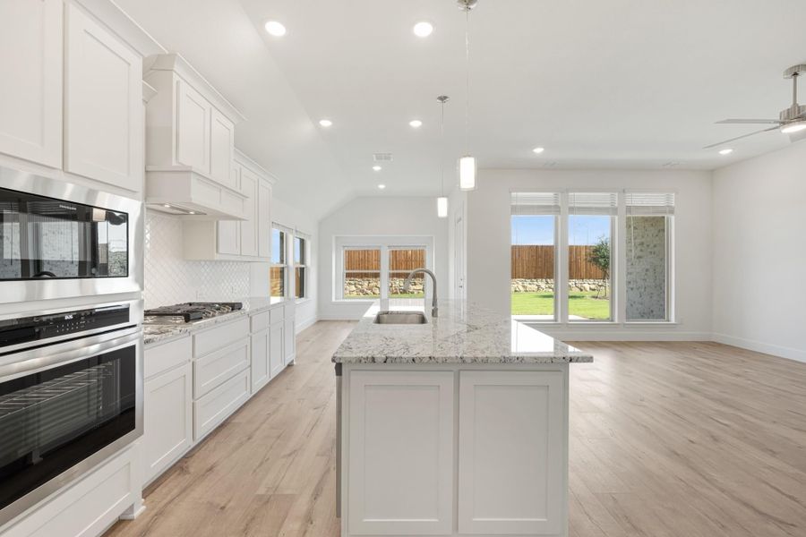 Open kitchen with white cabinets, granite island, stainless steel appliances, and light wood floors Open kitchen with white cabinets, granite island, stainless steel appliances, and light wood floors