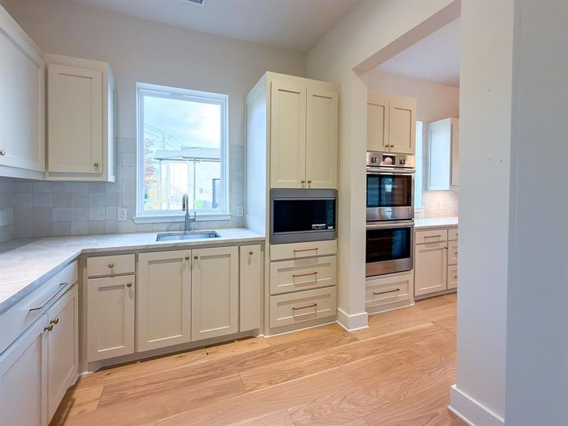 Kitchen featuring light wood-finish flooring, white cabinetry, light-toned countertops, a light-tiled backsplash, and stainless steel double ovens