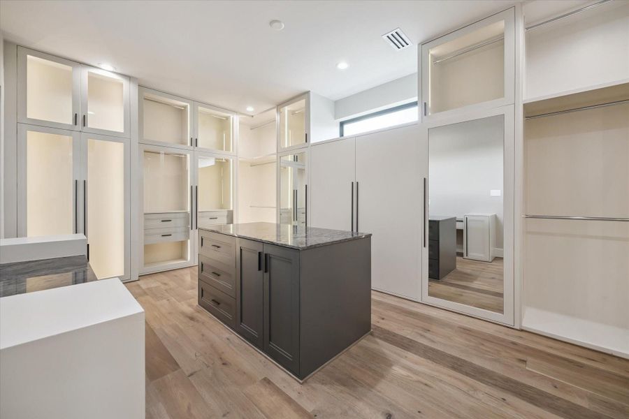 A central island with a quartz countertop provides additional storage and a stylish workspace, while full-length mirrors and warm wood flooring complete the luxurious dressing experience.