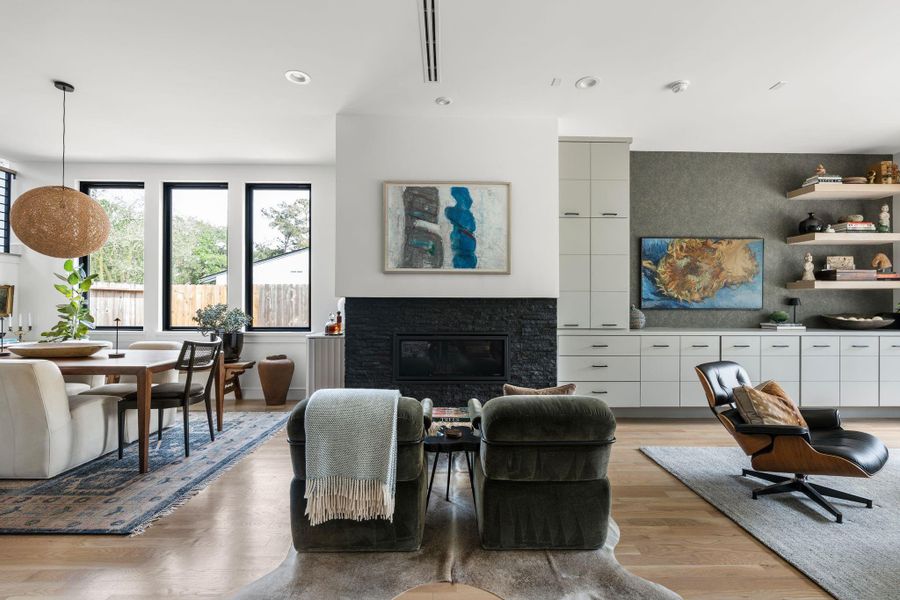 A stylish sitting area between the dining room and family room centers around a sleek fireplace with stacked stone surround and inlay accent lighting, adding warmth and definition to the open layout.