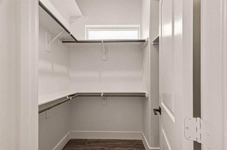 This photo showcases a well-organized walk-in closet with multiple shelves and hanging rods, featuring a small window for natural light. The space has a clean, modern finish with a neutral color palette and dark wood flooring. This photo showcases a well-organized walk-in closet with multiple shelves and hanging rods, featuring a small window for natural light. The space has a clean, modern finish with a neutral color palette and dark wood flooring.