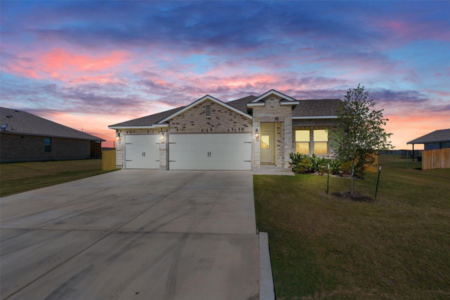 View of front of house with an attached garage, driveway, stone siding, a shingled roof, and brick siding