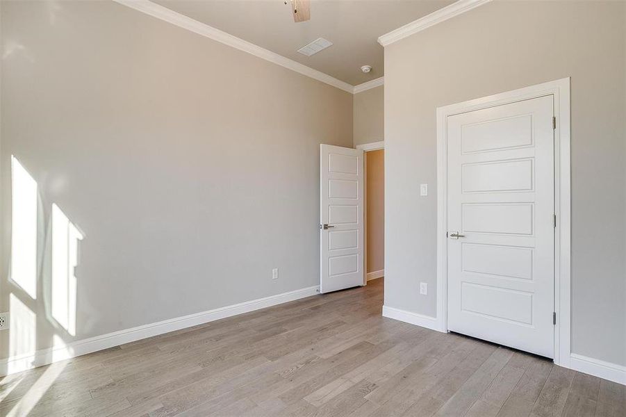 Empty room featuring a high ceiling, crown molding, ceiling fan, and light hardwood / wood-style floors