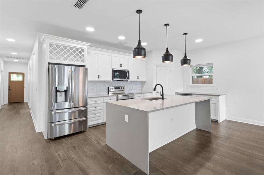 Kitchen with stainless steel appliances, light stone counters, backsplash, white cabinets, and decorative light fixtures