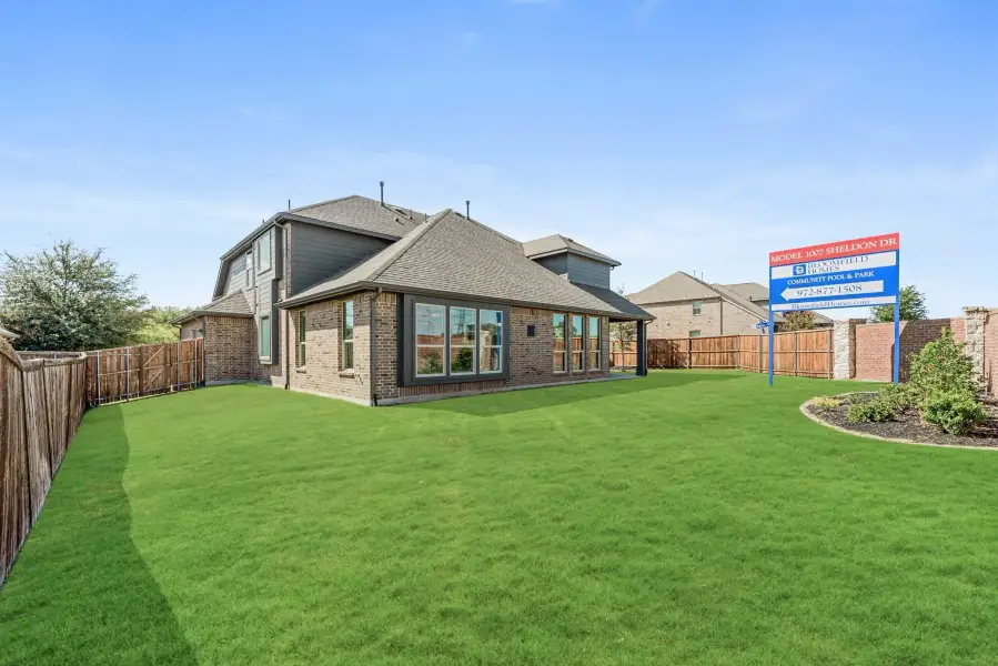 Rear view of two-story brick model home with large green backyard, wood fence, and Bloomfield Homes sign.