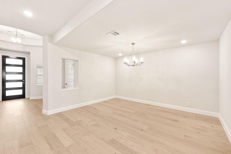 Empty dining room with light hardwood floors, chandelier, and view of entryway with black front door