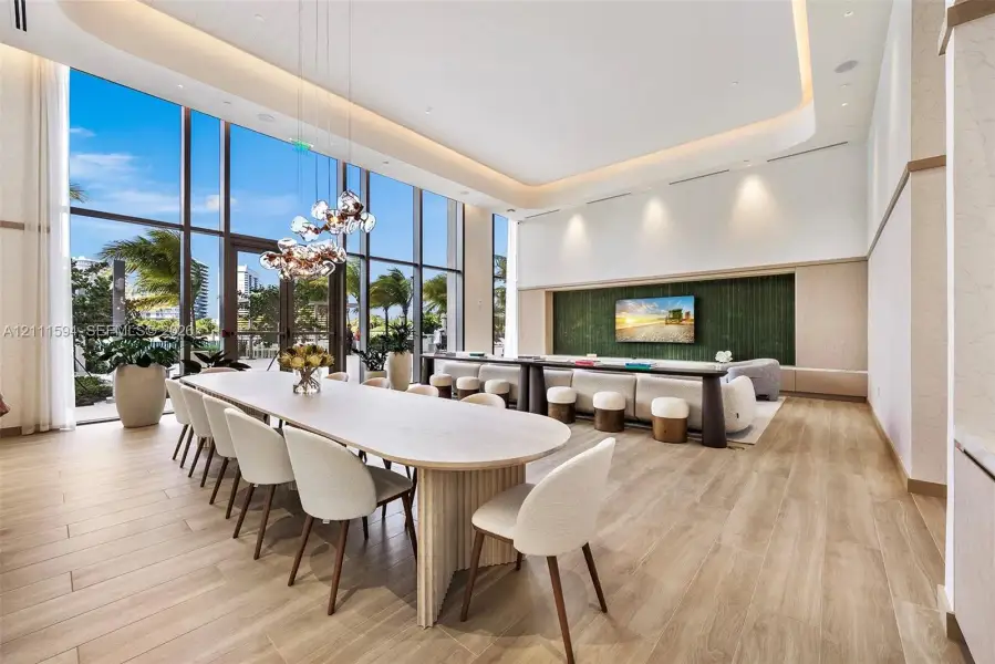 Expansive room featuring floor-to-ceiling windows, wood-finish flooring, recessed cove lighting, and a green textured accent wall with integrated cabinetry Expansive room featuring floor-to-ceiling windows, wood-finish flooring, recessed cove lighting, and a green textured accent wall with integrated cabinetry