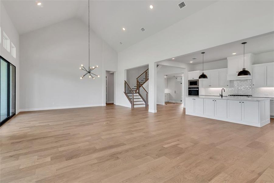 Unfurnished living room featuring high vaulted ceiling, light wood-type flooring, an inviting chandelier, and sink