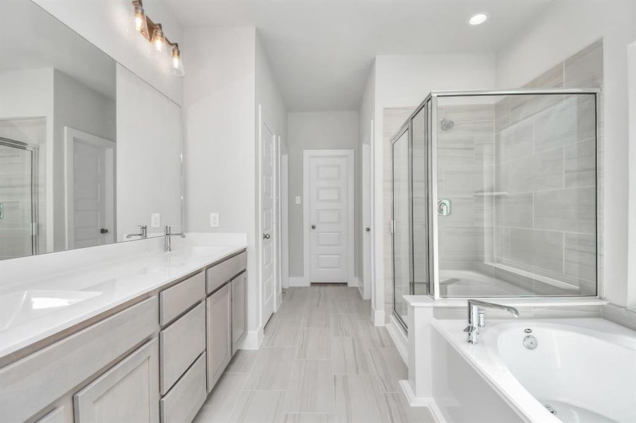 Escape to a spa-like oasis in this primary bathroom. Enjoy a walk-in shower with tile surround, a separate garden tub with custom detailing, and an elegant vanity featuring light countertops, modern hardware, and beautiful vanity lights. Experience luxury and relaxation in every detail.