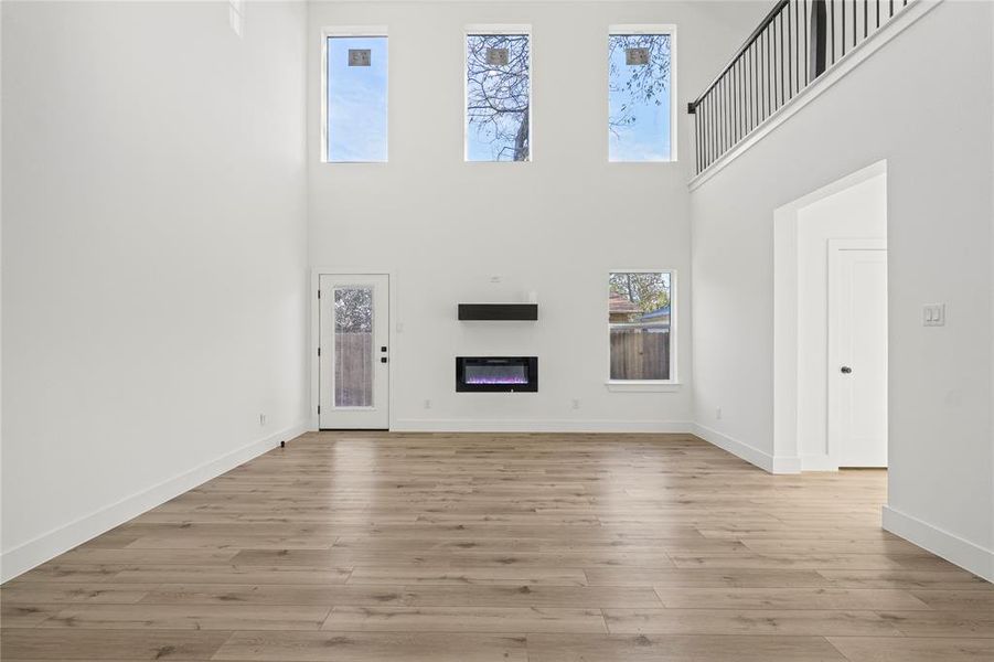 Unfurnished living room featuring a glass covered fireplace, light wood-style flooring, and a high ceiling