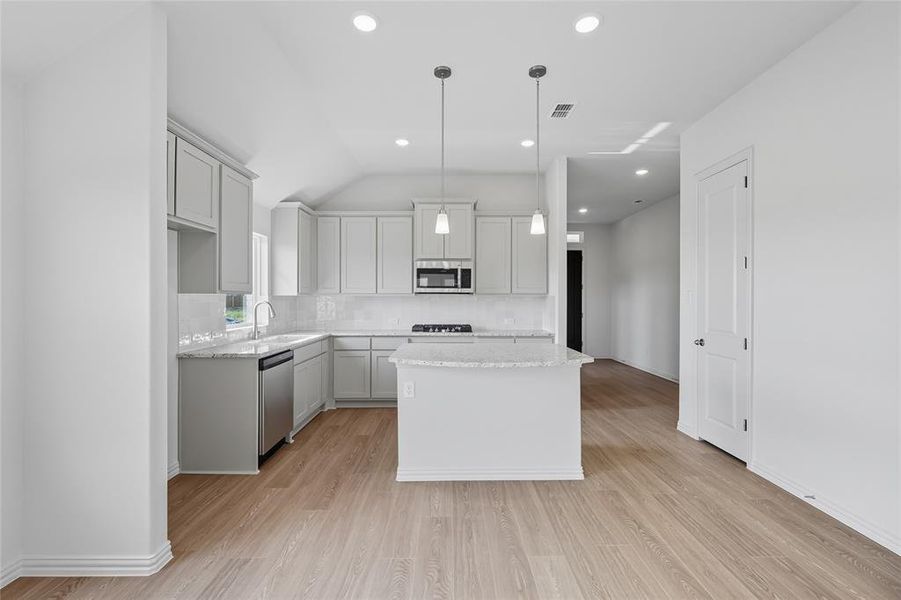 Kitchen featuring vaulted ceiling, light wood-type flooring, backsplash, a kitchen island, and hanging light fixtures Kitchen featuring vaulted ceiling, light wood-type flooring, backsplash, a kitchen island, and hanging light fixtures