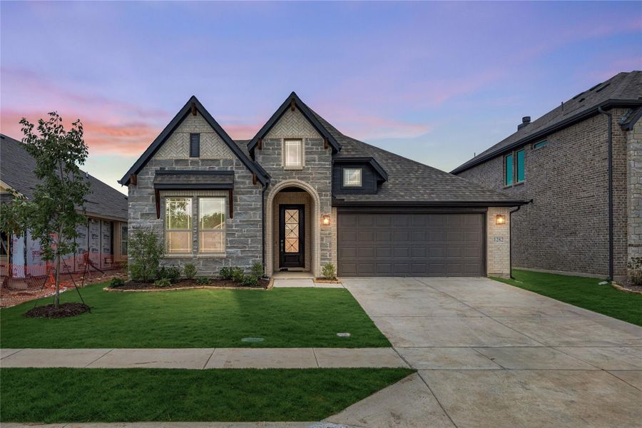 Single-story stone home with arched entry, two-car garage, and manicured front lawn at dusk