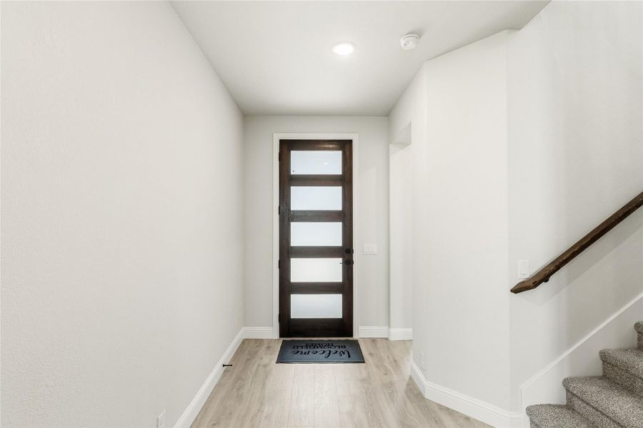 Entryway with dark wood front door with glass panels, light hardwood floors, and staircase with wood railing.