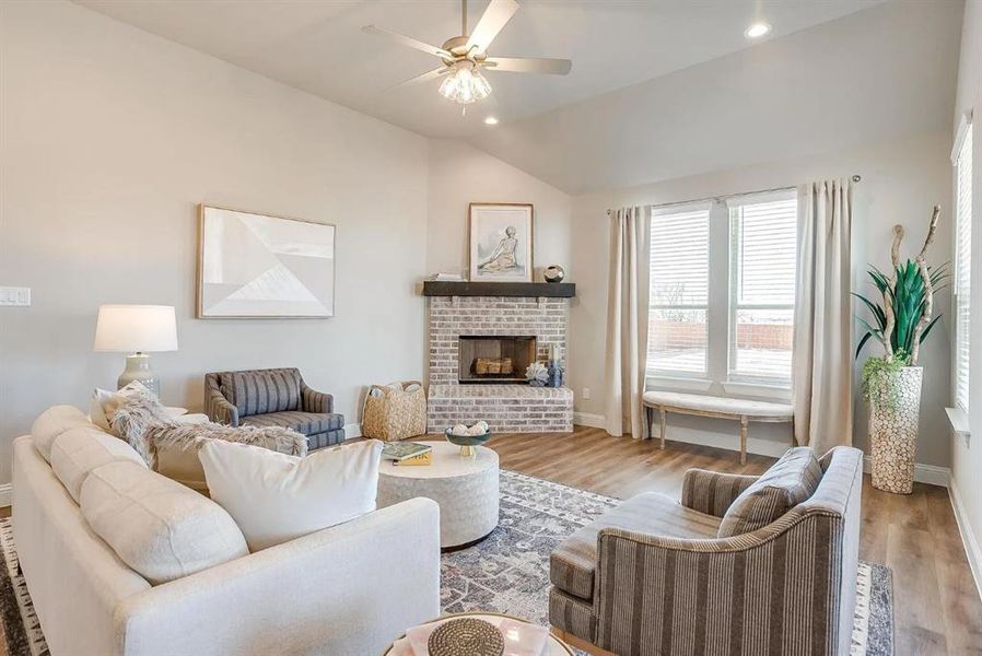 Living room featuring a brick fireplace, lofted ceiling, ceiling fan, and light hardwood / wood-style flooring