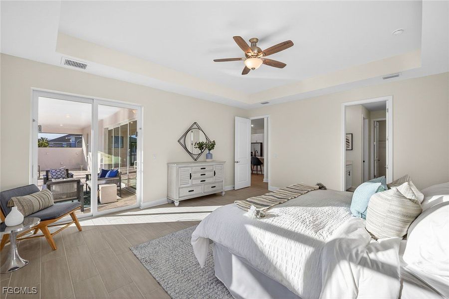 Bedroom with a raised ceiling, ensuite bath, ceiling fan, and access to exterior