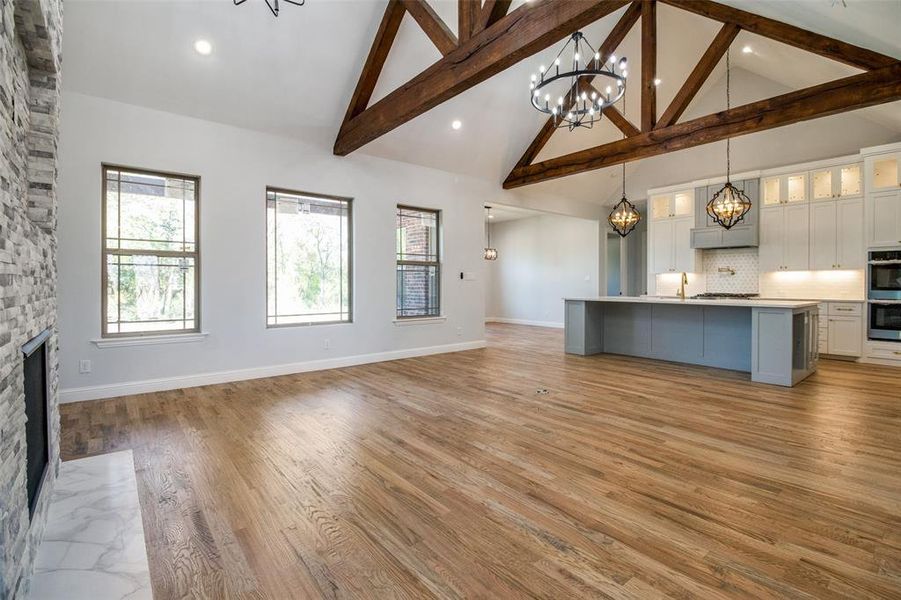 Unfurnished living room with beam ceiling, light hardwood / wood-style flooring, a chandelier, a fireplace, and high vaulted ceiling