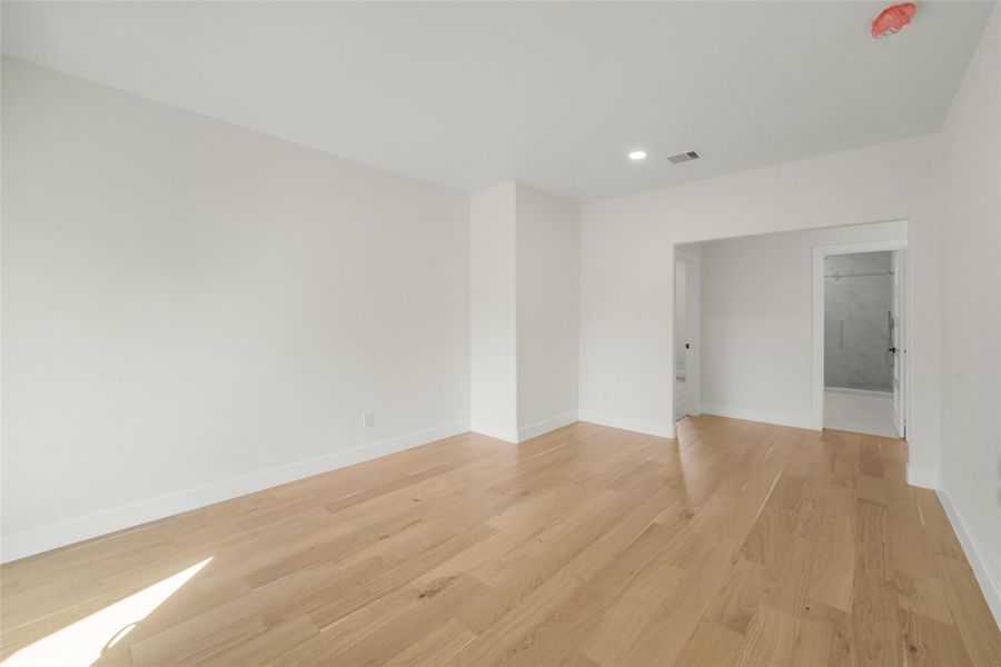 Bright, spacious room with light wood flooring and neutral walls. It features recessed lighting and an entryway leading to an adjoining bathroom with a glass shower door. Ideal for a bedroom or home office.