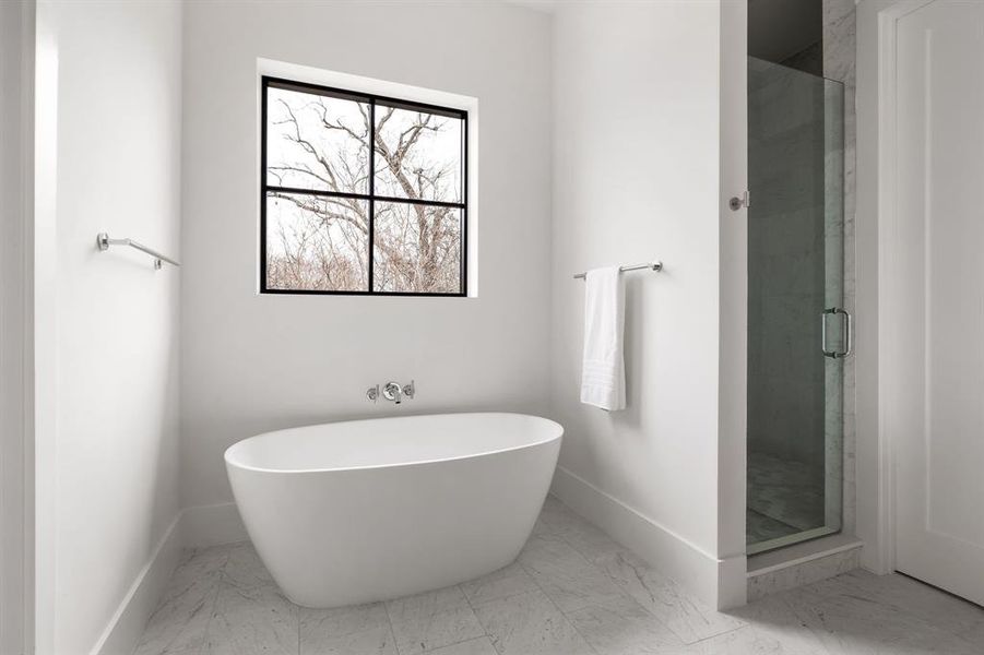 Full bath featuring marble finish floor, a freestanding tub, a shower stall, and baseboards