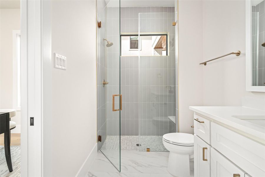 Stylish full bath featuring a walk in shower with vertical tile, frameless glass enclosure, and brushed brass fixtures conveniently accessible from the study or guest suit. Stylish full bath featuring a walk in shower with vertical tile, frameless glass enclosure, and brushed brass fixtures conveniently accessible from the study or guest suit.