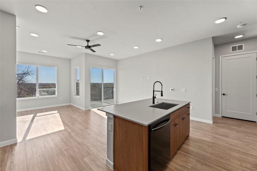 Kitchen featuring dishwasher, sink, a center island with sink, and light wood-type flooring