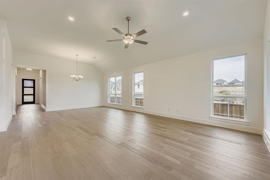 Unfurnished living room featuring light wood-style floors, recessed lighting, a ceiling fan, lofted ceiling, and a chandelier Unfurnished living room featuring light wood-style floors, recessed lighting, a ceiling fan, lofted ceiling, and a chandelier