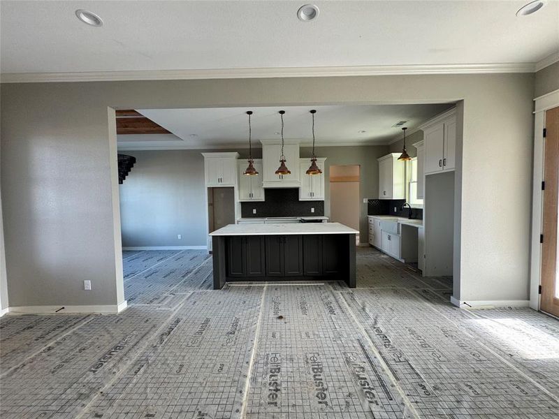 Kitchen with backsplash, crown molding, pendant lighting, white cabinets, and a center island