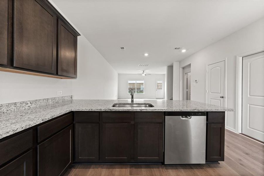 Kitchen with hardwood / wood-style floors, dishwasher, sink, dark brown cabinetry, and kitchen peninsula