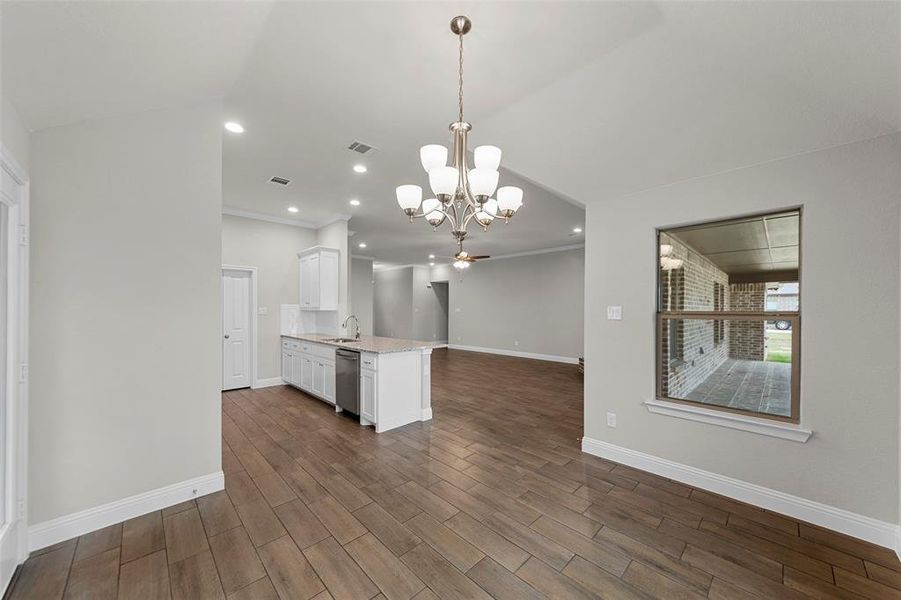 Open-concept living area featuring wood-finish flooring, a kitchen island with integrated sink, recessed lighting, and a decorative chandelier