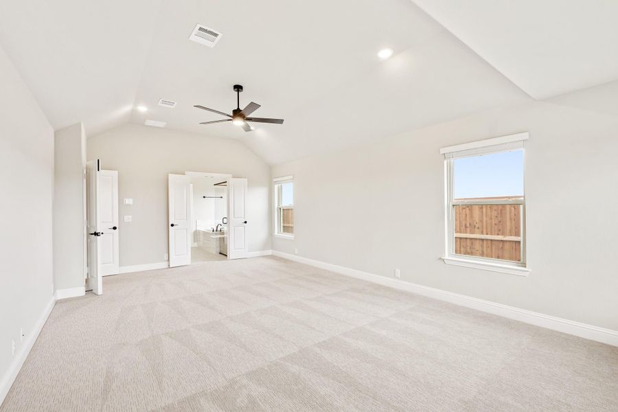 Spacious bedroom with vaulted ceiling, ceiling fan, carpet flooring, and ensuite bathroom doorway Spacious bedroom with vaulted ceiling, ceiling fan, carpet flooring, and ensuite bathroom doorway